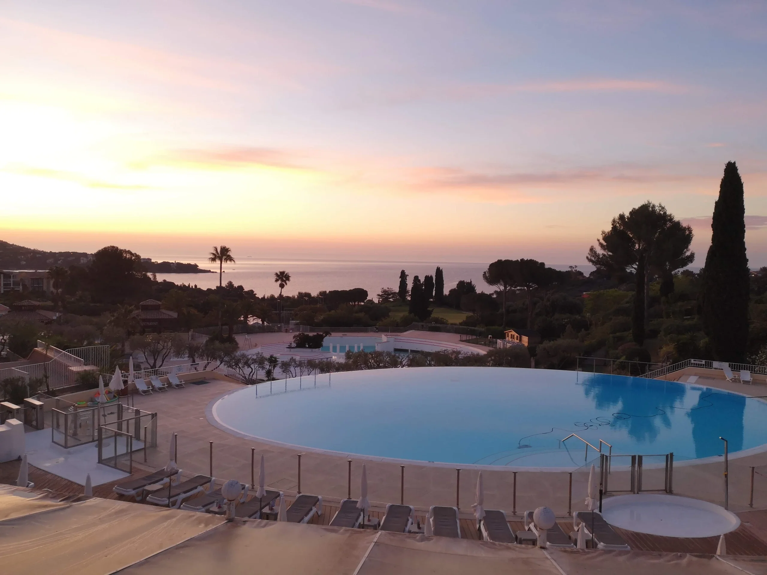 Piscines du domaine Cap Esterel, palmiers et mer sous un ciel rosé.